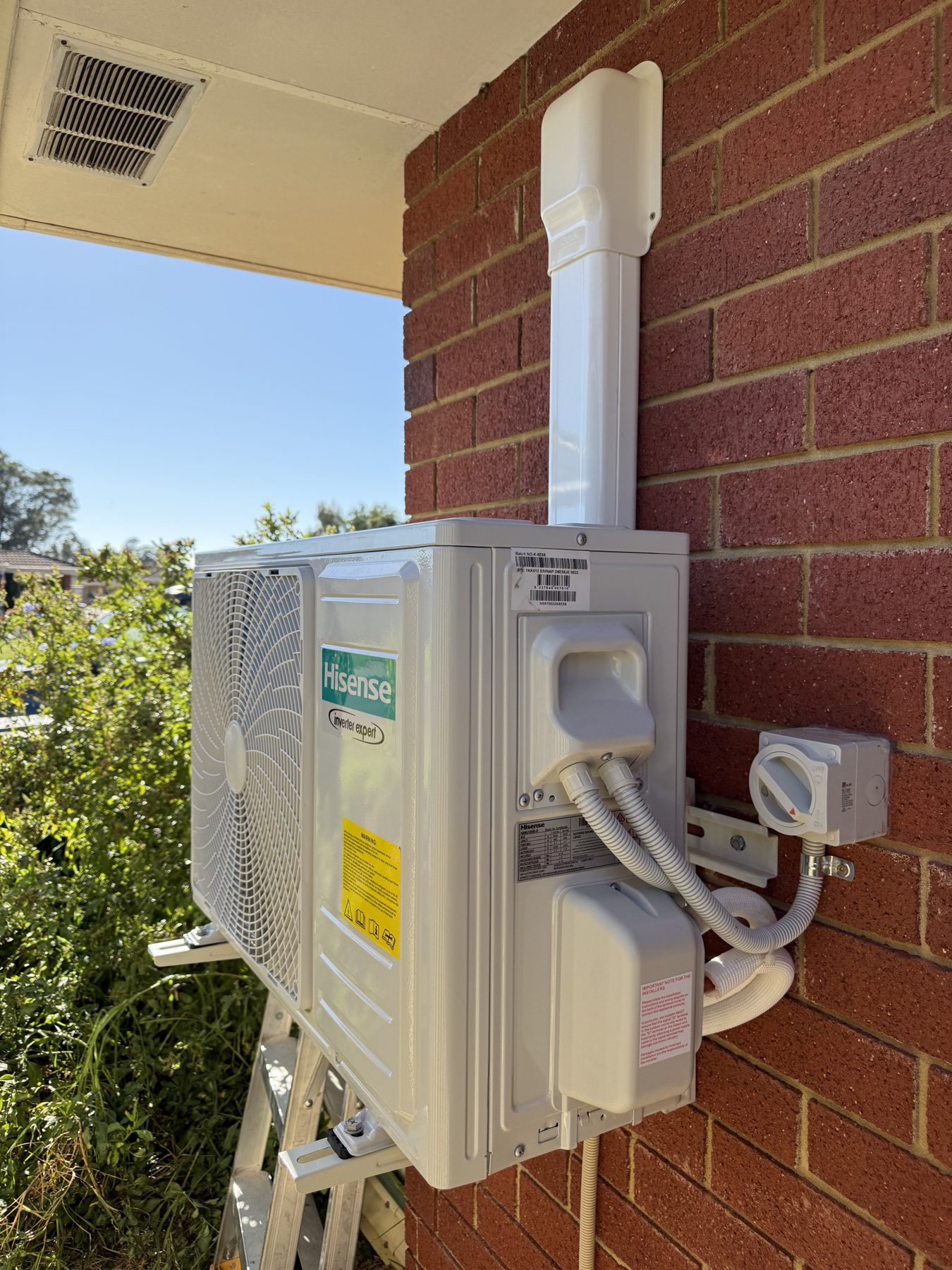 Outdoor split system condenser bracket-mounted to a brick wall with tidy pipework
